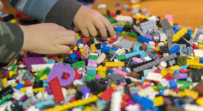 Close up of hands playing with colorful plastic bricks on the floor.